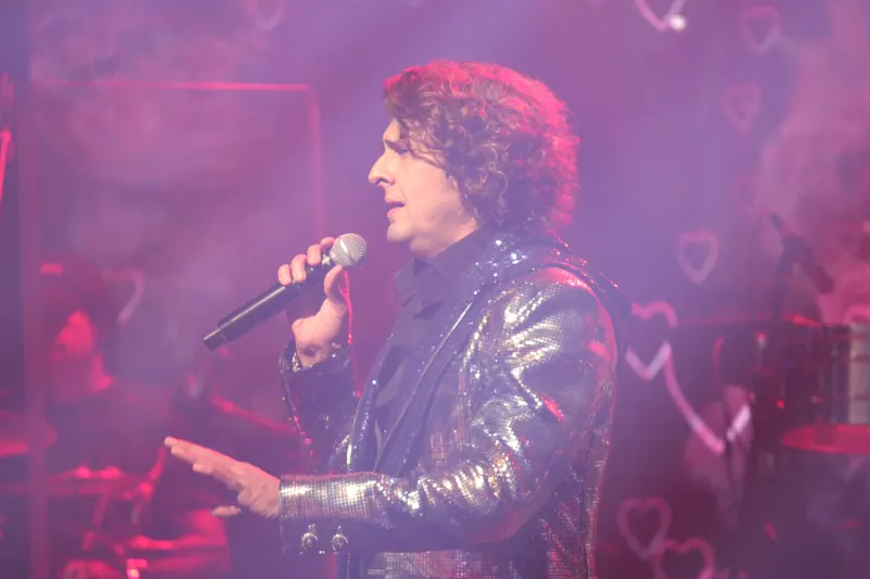 Singer in a metallic jacket through pink stage haze